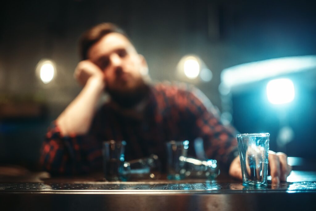 Drunk man sleeps at bar counter, alcohol addiction