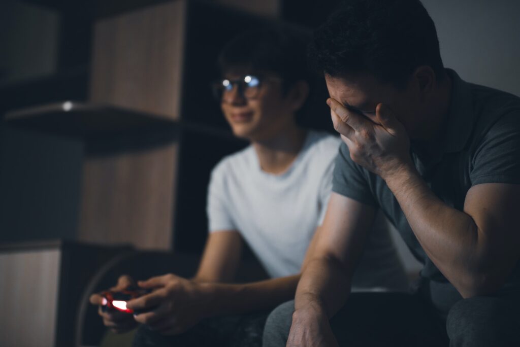 Emotional dad and son play on the console in the evening, sitting on the bed, dad was upset.