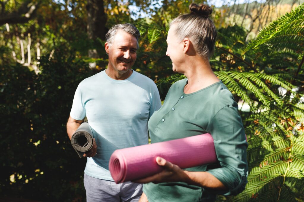 Happy senior caucasian couple practicing yoga, holding yoga mats in sunny garden