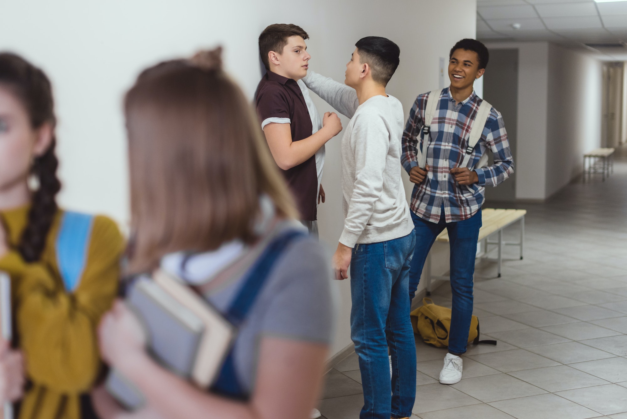 schoolboy being bullied by classmates in school corridor while schoolgirls passing away